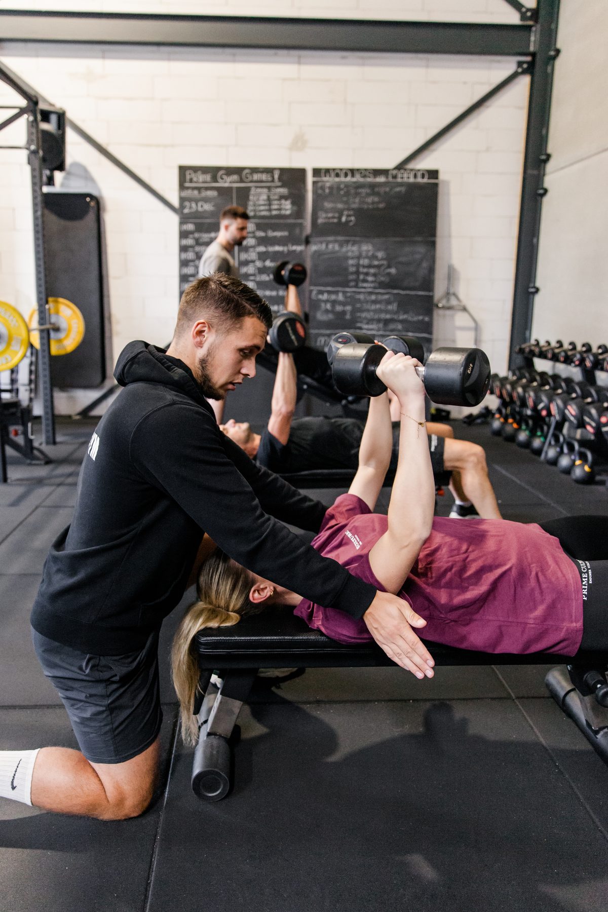 Personal training: een coach van Prime Gym begeleidt een lid bij de dumbbell press
